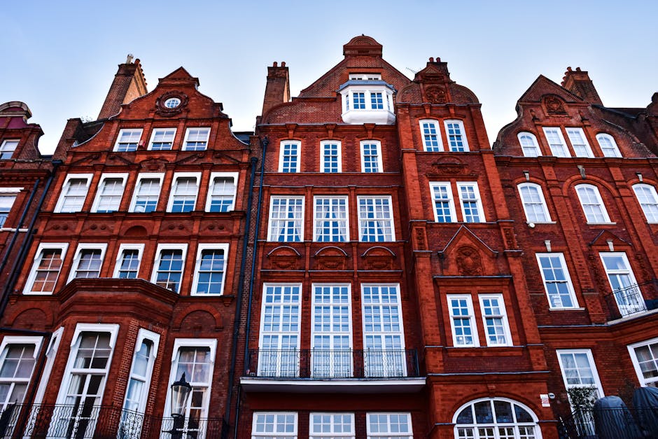 Photograph of a historic corner building on Marylebone High Street, with a rounded facade and large windows. The building has a light grey stone exterior with decorative architectural details at the roofline. A vintage-style sign hangs on the side, displaying the name 'The Marylebone' along with other faded text, indicating its historical significance. The ground floor features a storefront with a striped awning, and a small street sign indicating 'Marylebone Street W1' is visible. The building is illuminated softly by natural daylight, highlighting its classic design and well-maintained appearance. This image is relevant to the context of best cleaning tips for Marylebone High Street flats, as it depicts an iconic local structure, emphasizing the importance of maintaining historical and residential properties through expert cleaning services. Marylebone Cleaners specializes in comprehensive domestic and commercial cleaning, ensuring buildings like this remain pristine and well-preserved.