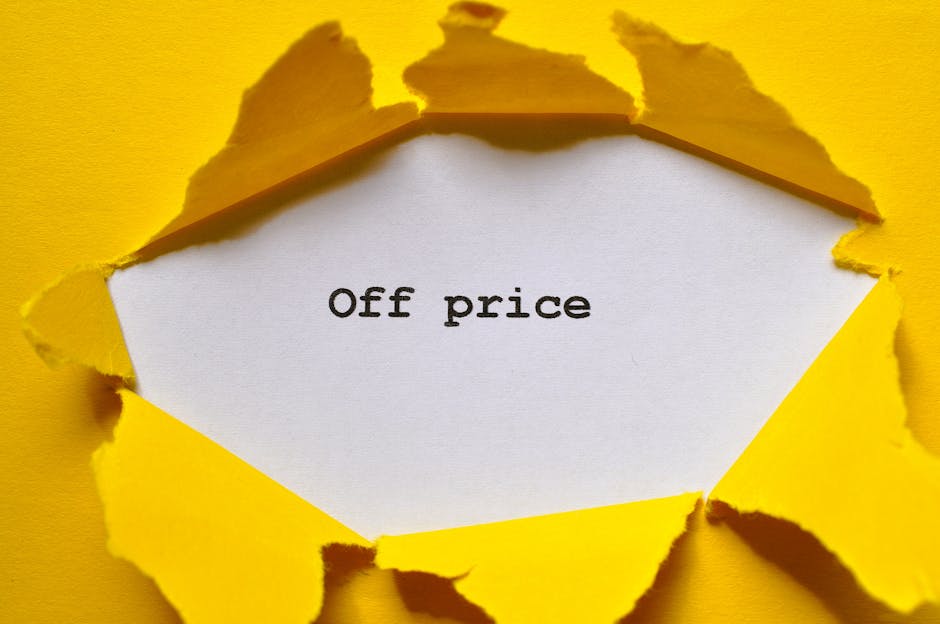 A torn piece of yellow paper reveals a white underlying paper with the phrase 'Off price' typed in black ink, situated in the center. The torn edges of the yellow paper curl outward, creating a jagged frame around the central message. The background is plain and neutral, emphasizing the contrast between the torn edges and the clean surface underneath. This image visually conveys the concept of discounted or reduced pricing, aligning with topics related to affordable surface cleaning or budget-friendly domestic cleaning services provided by Marylebone Cleaners, especially in the context of hidden pricing traps when booking a cleaner in Marylebone.